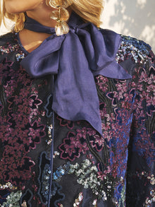 Close-up of a person wearing Social Queen’s Sequin Embroidered Velvet Mesh Jacket with a large matching bow at the neck and gold earrings—ideal for a chic party celebration.