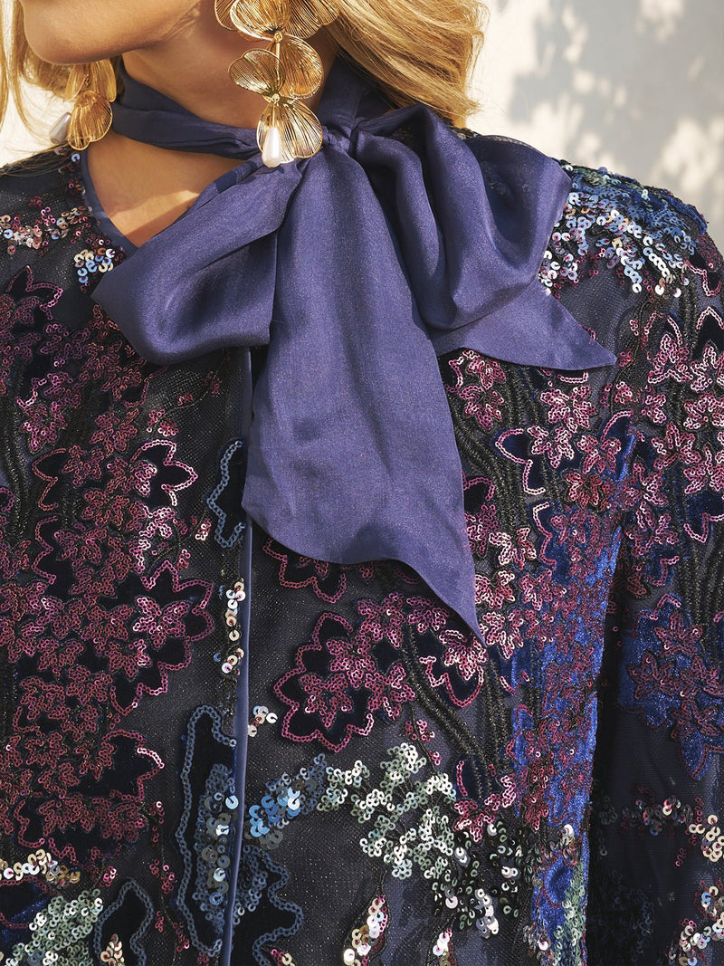 Close-up of a person wearing the Social Queen Sequin Embroidered Velvet Mesh Jacket, styled with a navy blue bow tie scarf and dangling gold earring.