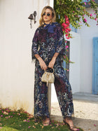 A woman in sunglasses wears the Social Queen Sequin Embroidered Velvet Mesh Jacket, holding a woven handbag while standing outdoors by a white wall with pink flowers and a blue door in the background.