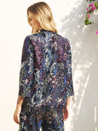 A woman stands outdoors facing away, wearing the Social Queen Sequin Embroidered Velvet Mesh Jacket; sunlight and pink flowers appear in the background.
