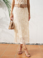 A woman wears the Social Queen Sequin Fringe Mesh Skirt with a tan belt, tan handbag, and gold sandals on a tiled floor against a white wall—showcasing fresh spring/summer style with subtle texture and chic flair.