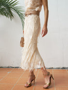 A woman in the Social Queen Sequin Fringe Mesh Skirt and a sleeveless lace top, paired with gold heels and a tan bag, stands on terracotta tiles by a white wall and palm leaf.