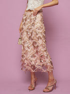 A person in a white lace crop top and the Social Queen Sequin Fringe Mesh Skirt stands against a pink background, holding a small gold purse.