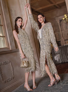 Two women wear Social Queen Sequin Fringe Side-Slit Midi Skirts with high heels, posing indoors and smiling while holding hands. One carries a small silver handbag; both have long, straight hair.