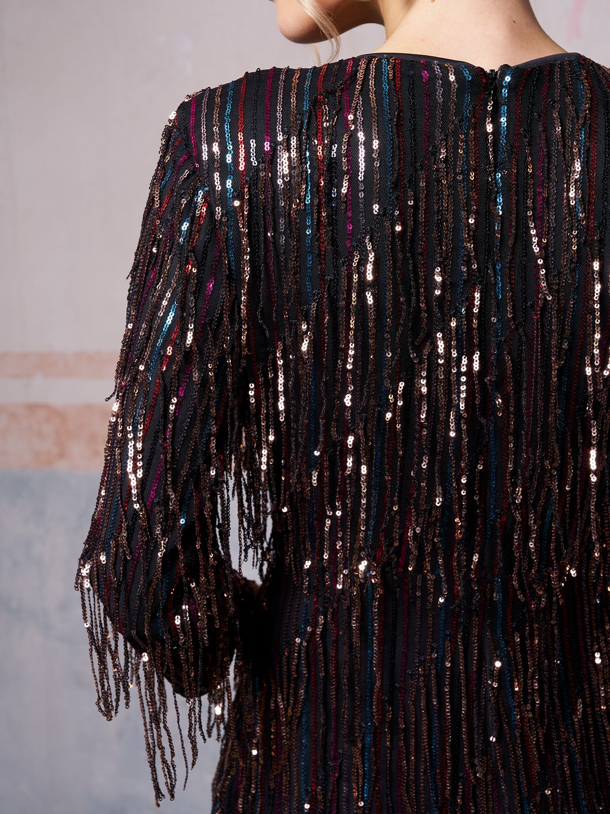 A person is wearing the Social Queen Sequin Fringe Slit Evening Gown, featuring long sleeves, vertical rows of shimmering sequins, and fringe detailing.