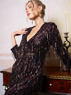 A woman wearing the Social Queen Sequin Fringe Slit Evening Gown poses beside a wooden table with ornate gold accents, a candlestick, and a faded wall in the background.