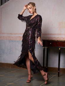 A woman wearing the Sequin Fringe Slit Evening Gown by Social Queen and high heels poses indoors beside a table, set against a textured wall.