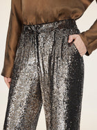A person stands with one hand in their pocket, wearing Social Queen’s Sequin High-Waist Wide-Leg Pants and a brown satin shirt.