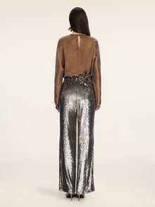 A person stands facing away, wearing Social Queen's Sequin High-Waist Wide-Leg Pants with a long-sleeve brown satin blouse and black high-heeled shoes.