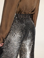 A person wearing a sheer brown blouse and Social Queen Sequin High-Waist Wide-Leg Pants with black and silver sequins, photographed from the back at waist level.