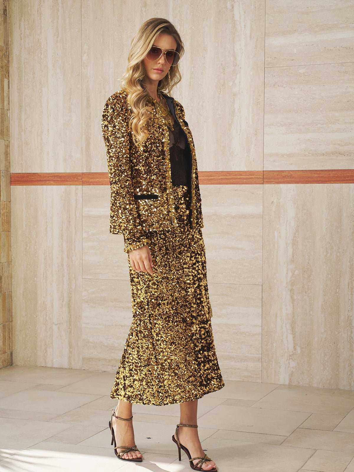 A woman in sunglasses and the Social Queen Sequin Velvet Skirt with a matching jacket stands indoors on a tiled floor, facing the camera.