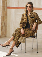 A woman in sunglasses and sandals holds a gold handbag while seated against a tiled wall, showcasing the Social Queen Sequin Velvet Skirt—ideal for adding sparkle to your next special event look.