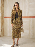 A woman stands indoors against a tiled wall wearing Social Queen’s Sequin Velvet Skirt, paired with matching jacket, sunglasses, a small gold handbag, and heeled sandals.