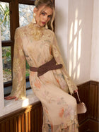 A woman sits on a windowsill in a sunlit room wearing the Social Queen Silk Floral & Bird Print Lace Dress—an elegant choice for wedding guests with its sheer sleeves and detailed design.