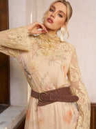 A woman poses indoors near a window wearing the Social Queen Silk Floral & Bird Print Lace Dress, featuring a high neck and long sleeves, styled with large earrings and a wide brown studded belt.