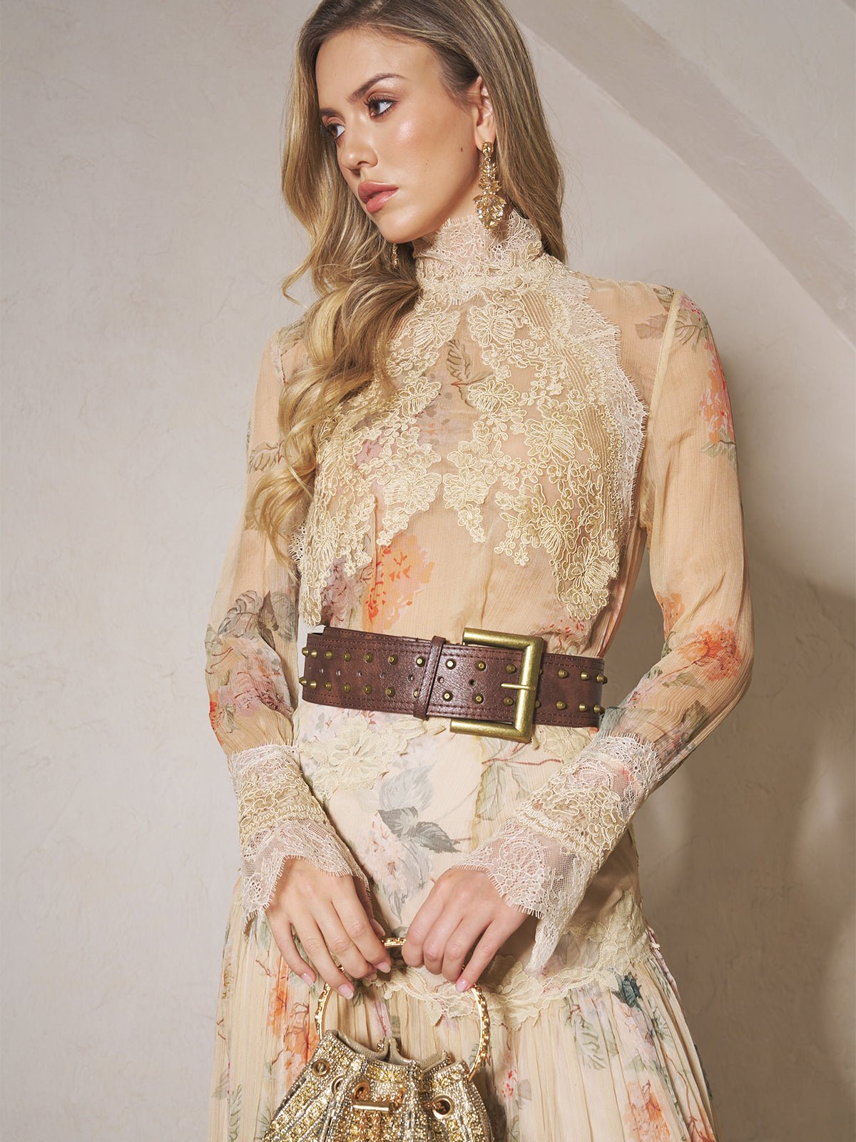 A woman wears the Social Queen Silk Floral Print Lace Blouse, styled with a wide brown studded belt and a small gold bag, standing against a neutral wall.