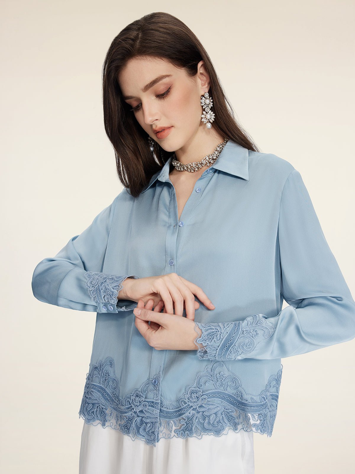 A woman wears the Social Queen Silk Satin Shirt with Lace Trim, styled with statement earrings and a necklace, standing against a plain background.