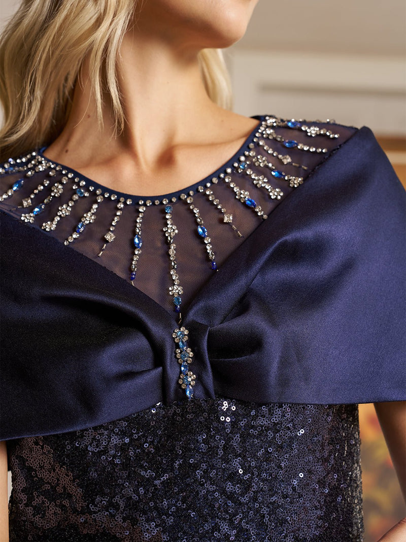 A woman wearing the Social Queen Starry Sequin Gown with Satin Bow Cape—an elegant navy evening dress with a sheer embellished neckline—makes a stunning choice for any wedding guest.