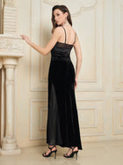 A woman wears the Social Queen Stretch Velvet Camisole with Embossed Lace—vintage-inspired, black with spaghetti straps and lace neckline—paired with black heels and statement earrings, standing indoors, her back partially turned.
