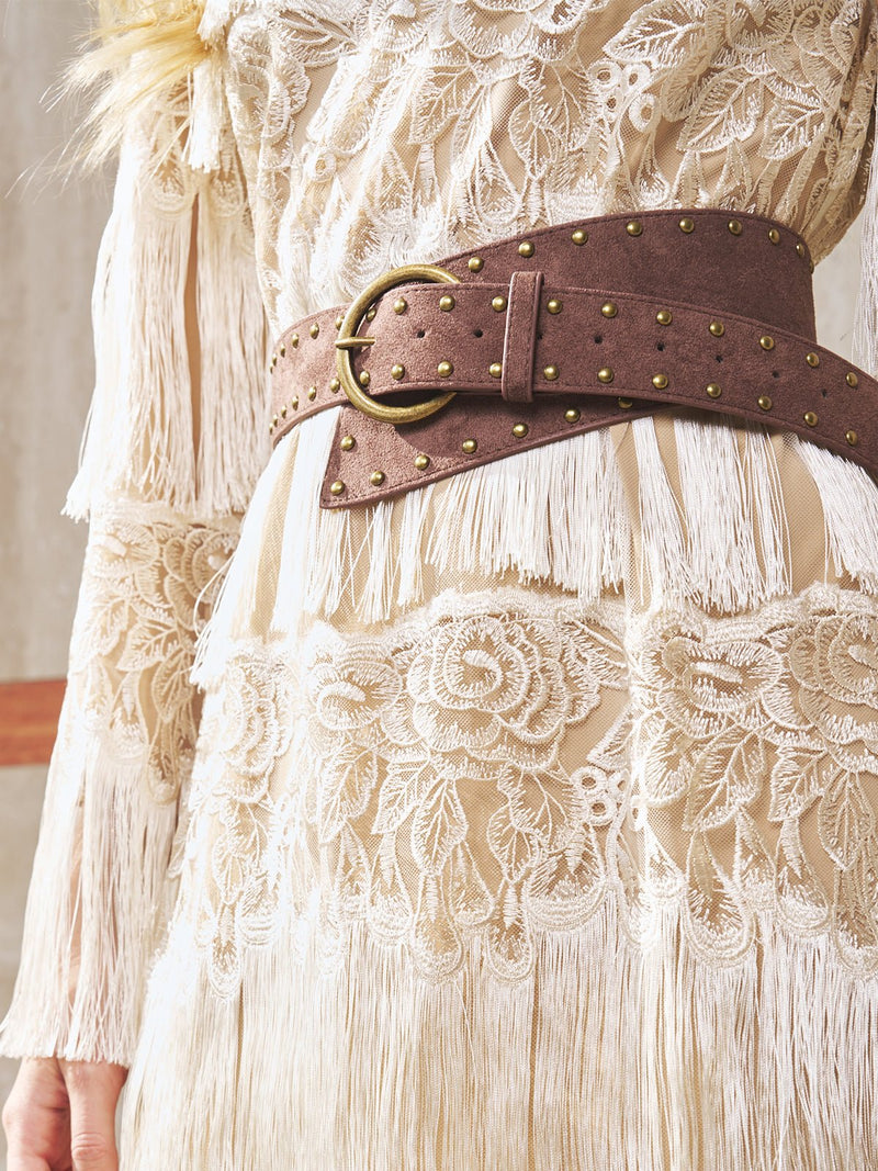 A close-up of a person in a cream lace dress with fringe details, accessorized with the Social Queen Studded Irregular Wide Suede Belt.