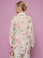 A woman with blonde hair in a bun faces away, wearing the Social Queen Textured Embroidered Beaded Shirt against a pink background, holding a beaded purse in her left hand.