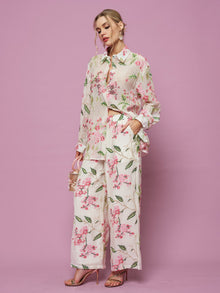 A woman wears the Social Queen Textured Embroidered Beaded Shirt with matching wide-leg pants, holding a small handbag against a solid pink background.