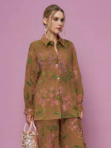 A woman poses against a pink background in the Social Queen Textured Embroidered Beaded Shirt, paired with earrings and a decorative handbag.