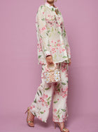 A person wears the Social Queen Textured Embroidered Beaded Shirt with matching pants, holds a small floral handbag, and pairs gold high-heeled sandals while standing against a pink background.
