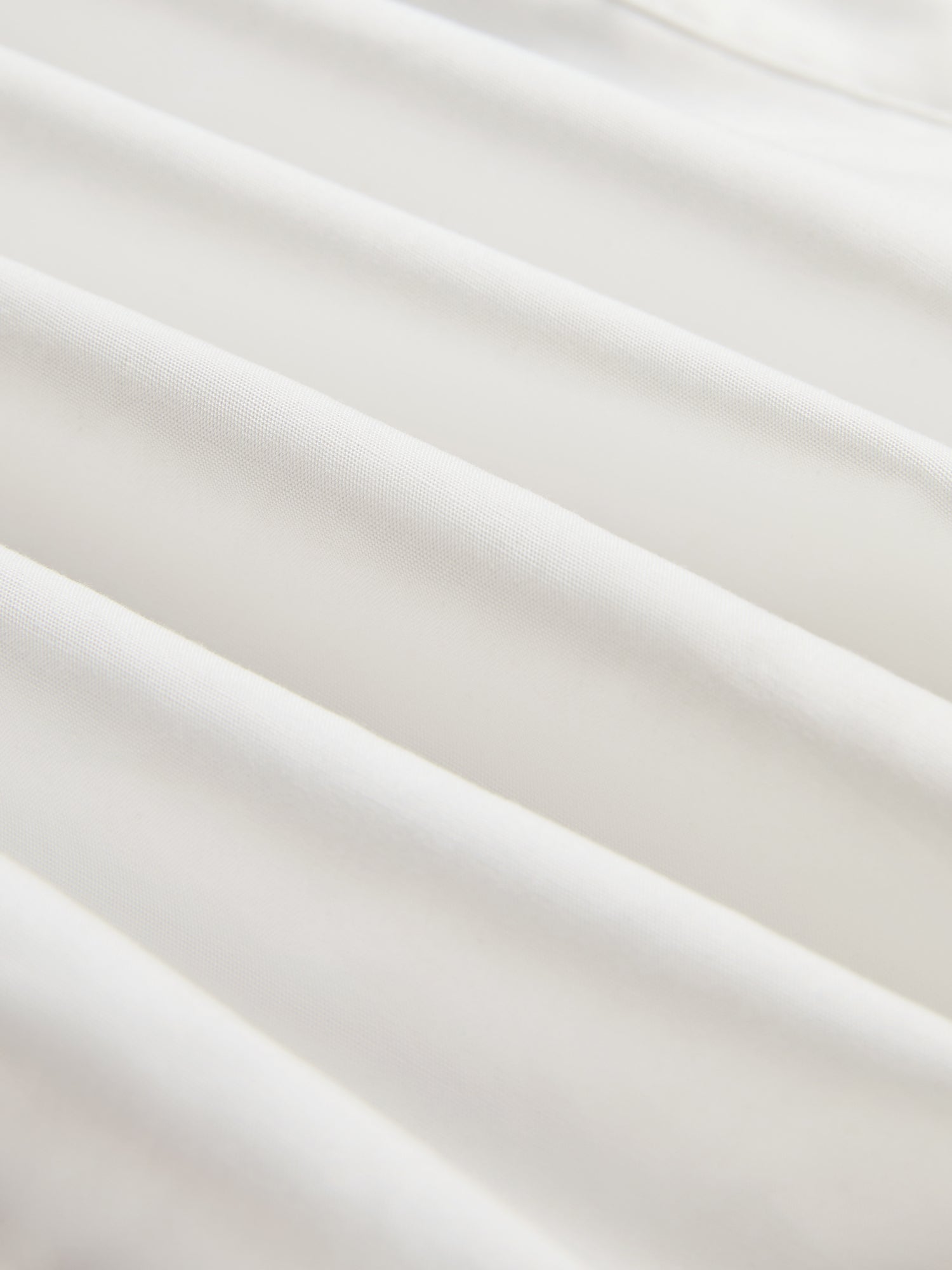 Close-up of smooth, white silk fabric with gentle folds and soft shadows, perfect for the Tie-Neck Silk Lantern Sleeve Blouse by Social Queen.
