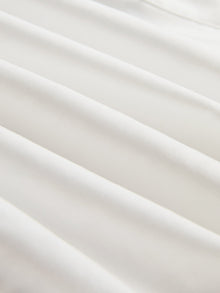 Close-up of smooth, white silk fabric with gentle folds and soft shadows, perfect for the Tie-Neck Silk Lantern Sleeve Blouse by Social Queen.