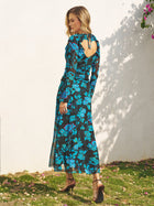 A woman stands outdoors wearing the Social Queen V-Neck Tie-Back Floral Knit Dress, featuring long sleeves, an open back, and ankle-length hem, paired with brown heels.