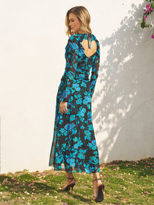 A woman stands outdoors wearing the Social Queen V-Neck Tie-Back Floral Knit Dress, featuring long sleeves, an open back, and ankle-length hem, paired with brown heels.