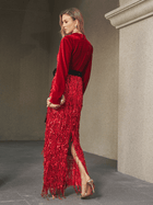 A woman stands in profile wearing the Social Queen Velvet Fringe Sequin Dress with a black belt, holding a clutch and high-heeled sandals in a stone hallway—an elegant wedding guest look.