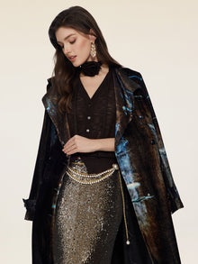 A woman wears the Social Queen Velvet Gradient Tie-Waist Trench Coat, paired with a black top, metallic sequin skirt, pearl belt, and statement earrings, standing against a plain light background.