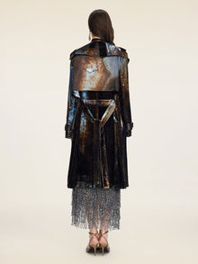A woman faces away in a Social Queen Velvet Gradient Tie-Waist Trench Coat, styled over a silver beaded fringe skirt and strappy heels, set against a plain background.