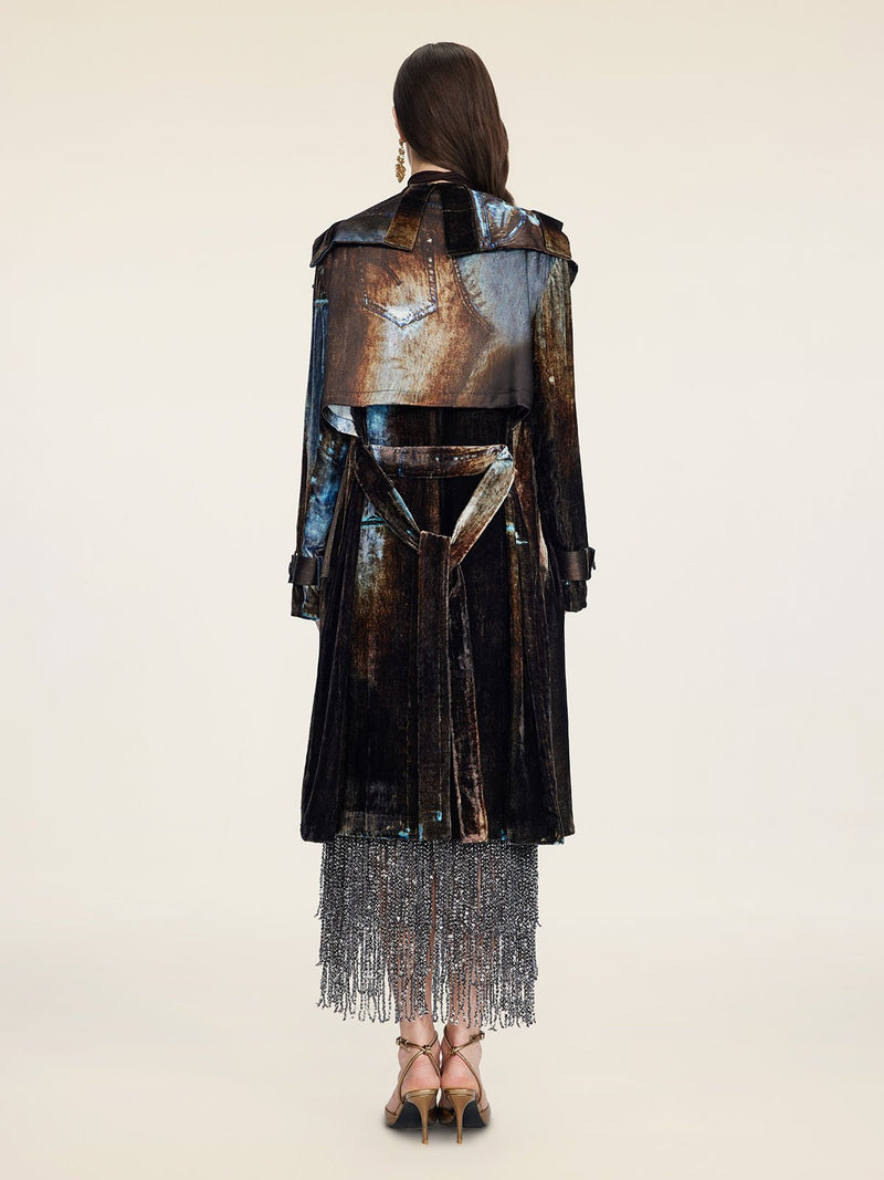 A woman faces away in a Social Queen Velvet Gradient Tie-Waist Trench Coat, styled over a silver beaded fringe skirt and strappy heels, set against a plain background.