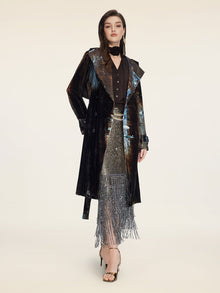 A woman poses in a studio wearing the Social Queen Velvet Gradient Tie-Waist Trench Coat, styled with a black blouse, metallic fringe skirt, and gold heels against a neutral background.