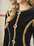 A woman wears the Velvet Jewel-Trim Dress by Social Queen, featuring black velvet with gold sequin trim, jeweled accents, metallic embroidery, and pairs it with long dangling gold earrings.