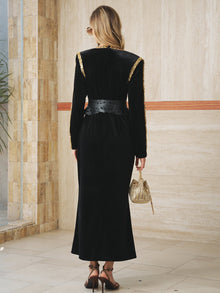 A woman wears the Social Queen Velvet Jewel-Trim Dress, stands facing away holding a gold handbag and wearing black sandals on a marble floor.