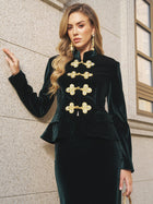 A woman stands against a stone wall wearing the Social Queen Velvet Knot-Button Jacket and a matching skirt, styled with gold earrings and a chain handbag.