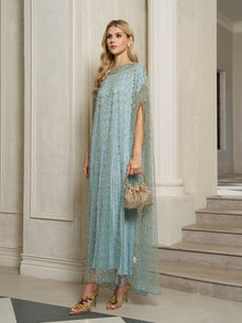 A woman stands indoors wearing the Social Queen Vertical Beaded Double-Layer Caftan Dress in light blue with gold accents, holding a small gold bag and pairing it with floral high-heeled sandals.
