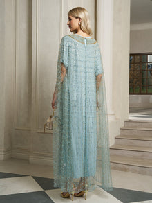 A woman wearing the Social Queen Vertical Beaded Double-Layer Caftan Dress in light blue stands indoors near a staircase, holding a small handbag and wearing gold high heels.
