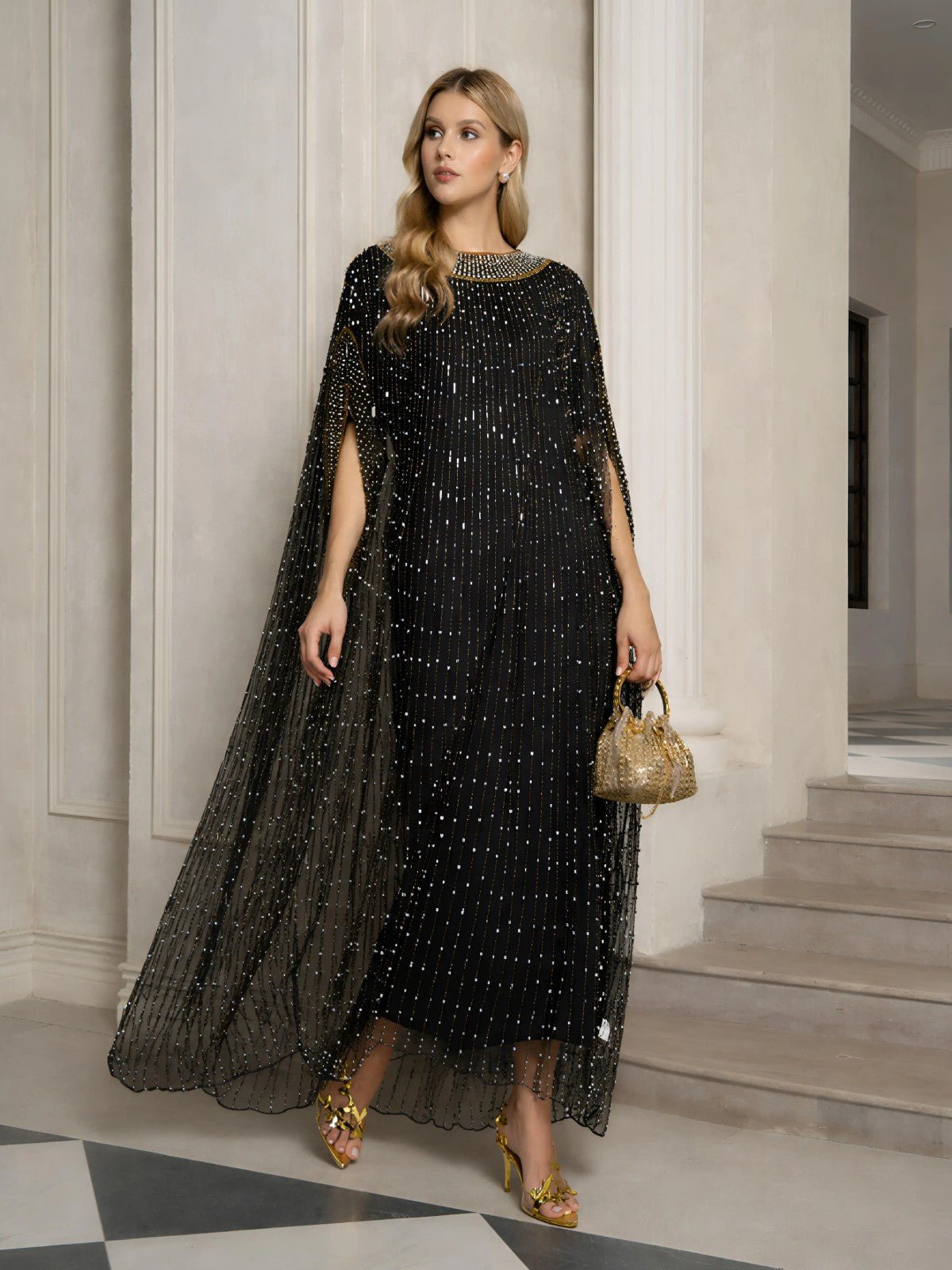 A woman stands indoors wearing the Social Queen Vertical Beaded Double-Layer Caftan Dress with a floor-length cape, gold sandals, and a small gold purse—the perfect party celebration outfit.