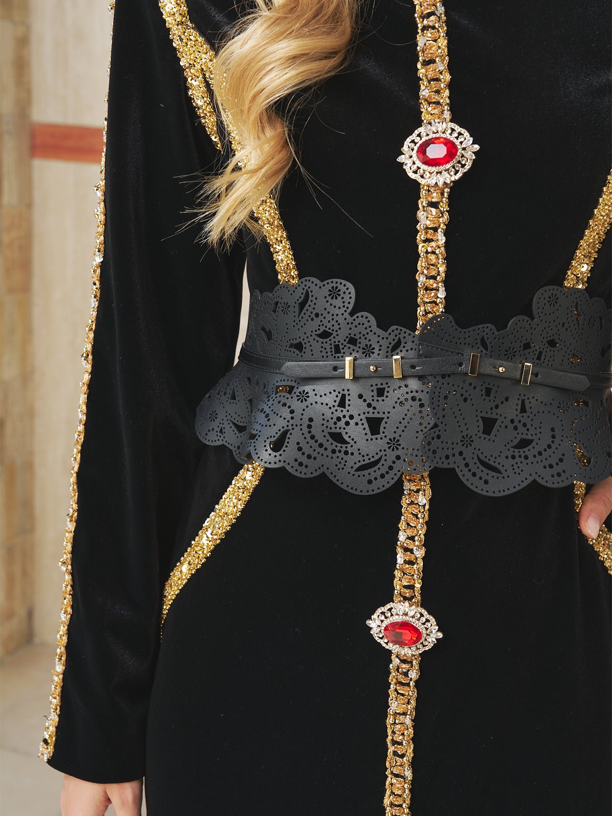 Close-up of a person wearing a black velvet outfit with gold sequined trim, red jeweled brooches, and the Social Queen Vintage Floral Cutout Waist Belt featuring decorative floral cutouts.