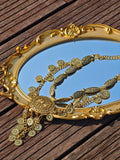 The Social Queen Vintage Sunflower Necklace is displayed on an intricately framed oval mirror atop a wooden surface, highlighting its ornate gold sunflower charm.