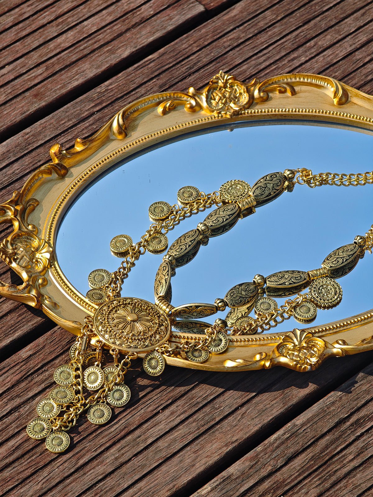 The Social Queen Vintage Sunflower Necklace is displayed on an intricately framed oval mirror atop a wooden surface, highlighting its ornate gold sunflower charm.