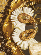 Social Queen’s Woven Fan-Shaped Earrings feature cream fringes and floral cutouts, elegantly displayed on an ornate gold tray.